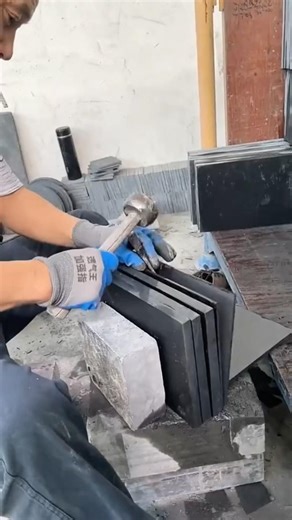 Chiseling one thick black granite block into paving stones and wall cladding with the same thickness