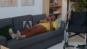 Middle-aged man with disability using mobile phone when lying on sofa