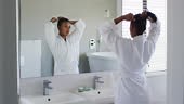 African american woman in bathrobe tying her hair looking in the...