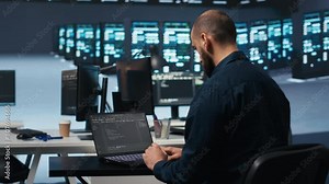 Computer scientist using laptop device to do programming in data center room housing servers . IT supervisor writing code on notebook to mend data storage facility racks doing computational operations