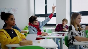Estudiantes de secundaria prestando atención en clase, sentados en sus escritorios y levantando la mano.