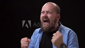 portrait of bald bearded angry screaming man on black background. guy is upset and angry and emotionally unstable. Man in blue shirt with negative emotions.