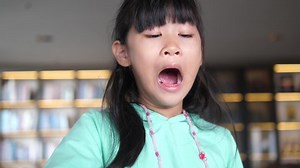 Schoolgirl girl yawns while sitting at the table doing homework at home. A tired female student studies
