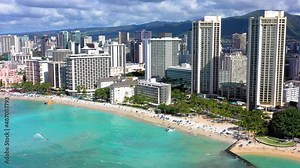 Drone view of Waikiki beach in Honolulu Hawaii with a large sailboat, beach goers, palm trees and beautiful clear water.