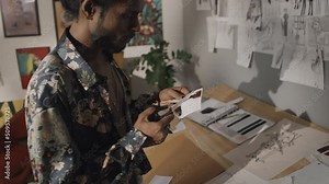 Talented Indian fashion designer cutting out small print sample with scissors, working in creative mess in retro style studio Stock Video