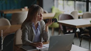 Asian woman talk on cell using voice assistant. Woman sitting on couch holds phone talks on speakerphone with friend makes voice recognition or request uses internet services through virtual assistant