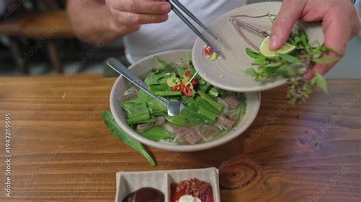 Spicy Chili Served. Red Chili And Herbs Enhance Soup Flavor. Chopsticks Place Fresh Chili Into Hot Pho Bowl. Rustic Table Hosts Diner Carefully Adding Chili And Herbs To Pho