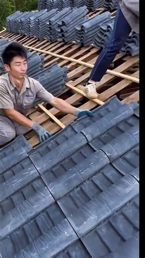 Installing dark ceramic roof tiles on a wooden frame during house construction