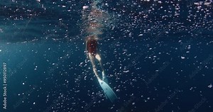 Free diver woman relaxing after diving with fins in blue ocean with bubbles. Underwater view
