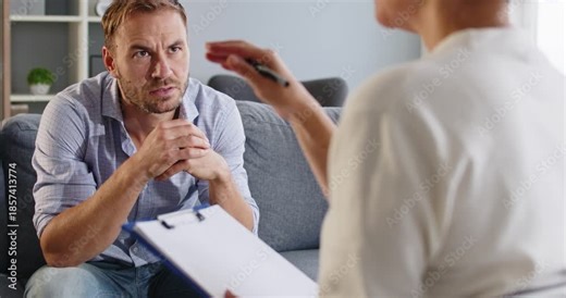 Therapist counseling patient man during therapy session. Advisor notes on a clipboard while client discusses stress and goals in a calm office. Mental health support and counseling concept.
