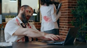 Creepy looking office zombie working on laptop while smirking bizarre at camera. Dangerous brain dead monster with bloody and deep scars and wounds trying to use computer but fails.