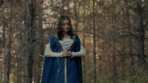 Beautiful model in a form of elf princess walking in the forest with small bouquet of wild flowers. Elvish princess greets the woods.