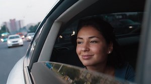 A young beautiful woman rides in a taxi with an open window, smiles, takes a photo of the street on her phone. Road, trip, car. Slow motion 4k footage