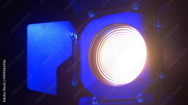 Theater spotlight with a fresnel lens with curtains on a black background with blue reflections, turning towards the camera. Medium plan