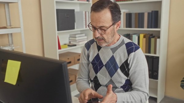 Man reading document at computer, frowning and holding paper while wearing glasses in building; worry bills finance Stock Video Footage - Alamy