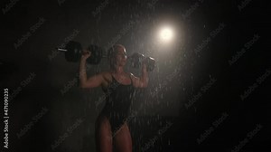 The fitness model is standing in the shower and doing a shoulders exercise. She is doing a dumbbell press over her head. Water is running down her body. 4K 50fps