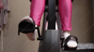 Woman cycling on an exercise bike, close-up of legs, indoor fitness routine, healthy lifestyle