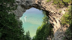 Arch Rock on Mackinac Island, Michigan. Docked boat with swimmers in turquoise Great Lakes waters visible through the arch.
