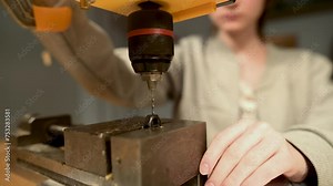 Young pretty female operating a drill press in the workshop crafting handmade jewelry. Original jewellery craftsmanship, hand-made bijouterie making. Working table close-up.