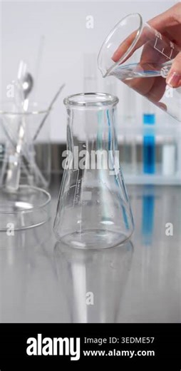 Close-up of a chemist pouring a transparent liquid from a glass beaker into an erlenmeyer flask on a stainless steel table in a lab Stock Video Footage - Alamy