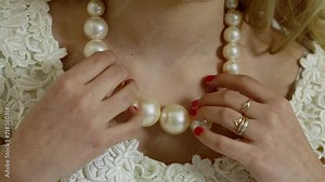 Woman fingers touch artificial pearl necklace and white dress