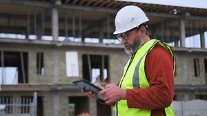 Construction worker using digital tablet on building site, civil engineer checking construction blueprint, side view, professional inspect, blurred background.