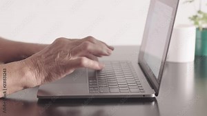 Close up shot of hands of retired old woman ( grandmother ) using laptop at home in the living room. Elderly business woman seating on the table, and typing the text on modern PC. Online technology