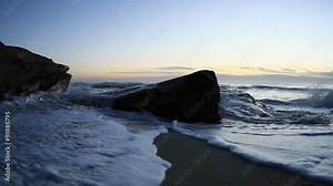 A hand held camera captures waves rolling on to a beach just after sunset.