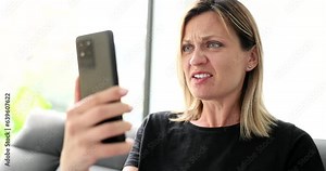 Embarrassed annoyed girl client and using smartphone at home reading message. Negative notification feeling dissatisfied looking at phone