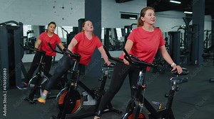 Athletic women group making stretching training on spinning stationary bike routine in gym. Girls make workout fitness cardio on exercise cycling bike indoors. Weight loss, fat burning. Modern sport