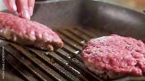 Cook metal spatula turns meat burgers, which are fried in a frying pan grill with non-stick coating in boiling, splashing olive oil. Fried brown crispy crust. The process of cooking in the kitchen.