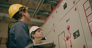 Two electricians electrical engineers in protective uniform checking voltage control panel screen system at electrical cabinet for generate electricity of factory in manufacture industrial