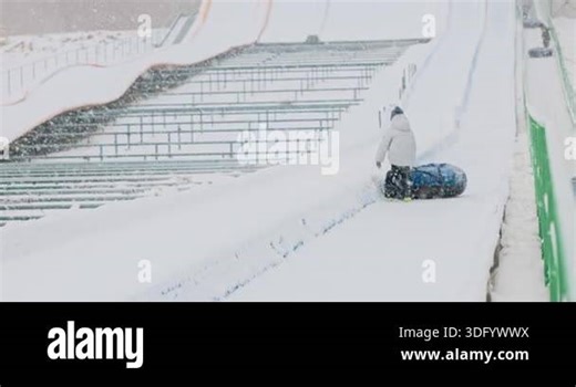 A person in winter attire slides down a snowy slope on an inflatable tube. The scene captures the excitement and fun of snow tubing in a winter wonderland setting Stock Video Footage - Alamy