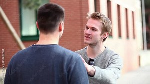 Two men talking and laughing together. Young friends standing face to face and enjoying time together. Urban city life situation with real people. Friendship and lifestyle concepts.
