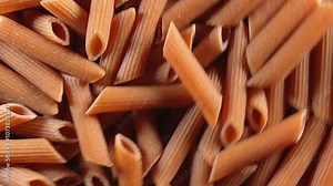Uncooked Whole Grain Penne Rigate Pasta: A Culinary Canvas of Whole Wheat Macaroni, Textured Background - Top View, Rotating. Turning Whole Grain Dry Pasta. Whole Wheat Raw Macaroni - Angular Rotation