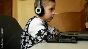 Boy 5-6 years old in headphones looks at a laptop monitor screen. Children and electronic devices