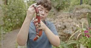Teenage girl holding her pet snake in a garden, focus on the snake.