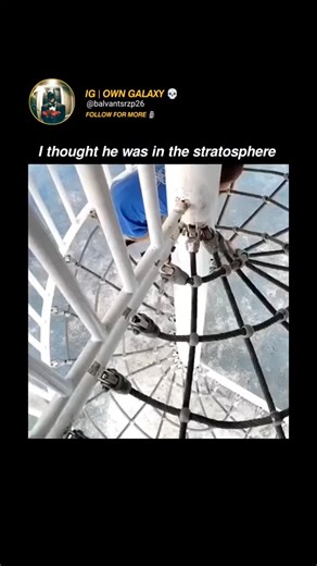 OwnGalaxy🥶 on Instagram: "This Instagram Reel depicts a young Asian boy, approximately 4-5 years old, dressed in a blue graphic T-shirt and sandals, methodically climbing a tall spiral staircase constructed from white cargo netting. The structure appears suspended over a blue-tinted surface, possibly a pool or padded area, creating an optical illusion of extreme height against a bright outdoor setting with red flooring and white railings. The footage captures his determined hand-over-hand ascen