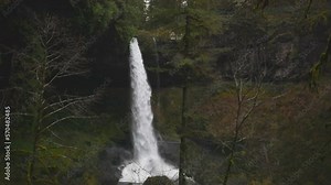 Fast gushing Silver Falls Oregon flowing rain forest waterfall with water crashing at bottom on top of rock under dark early morning. Full view from the side with water crashing on top of bottom rock