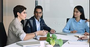 Serious confident Middle Eastern business woman speaking at negotiation meeting, talking to multiethnic team of partners, sitting at large table, discussing teamwork, agreement, cooperation