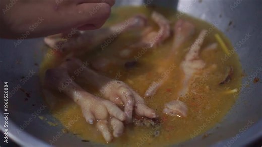 Human hand placing chicken meat into hot broth in a pan, close-up cooking process of poultry simmering in seasoned soup for homemade cuisine.