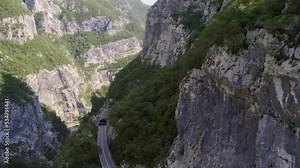 Traffic road with moving trucks coming out of a tunnel in a river gorge shot on a sunny day from the air by a moving drone passing by the canyon cliffs