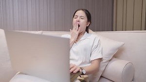 Pretty asain woman yawning while get online with laptop computer sitting on comfortable sofa, work exhaustion late at night, sleepy tiring working woman inside home workspace, not enough rest