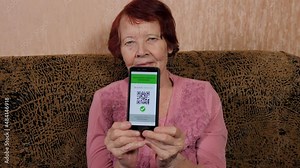 Elderly grandmother showing electronic passport of a vaccinated person against covid-19, qr-code on screen of mobile phone, close-up. Selective focus on health passport Covid 19.