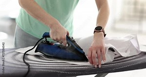 Woman hands are ironing collar of white shirt on ironing board. Ironing clothes