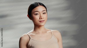 Beautiful person creating skincare cosmetics ad, posing with glamour and tenderness on camera. Asian woman promoting beauty products for radiant luminous skin, body acceptance.