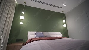 A cozy bedroom with a green accent wall, modern pendant lighting, and a comfortable bed dressed in soft linens