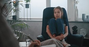 Asian school-aged girl sits in chair, talks to child therapist, shares feelings during therapy. School psychologist takes notes, provides counseling session for kid. Psychology concept. Psychology.