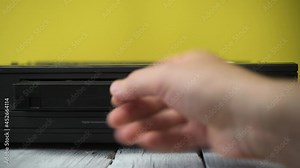 A hand inserts a video cassette into an old VCR.