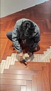 Installing wooden floor with herringbone pattern using hammer and wooden block for tight fit